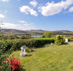 A garden with a small wishing well flowers and bushes with hills and a lake in the background at LOCH ILLION VIEW in Dungloe County Donegal