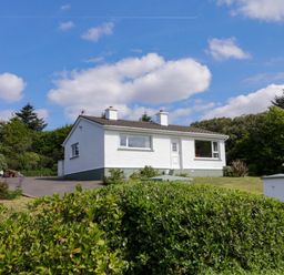 A small white house with two chimneys surrounded by a garden and greenery at LOCH ILLION VIEW in Dungloe County Donegal