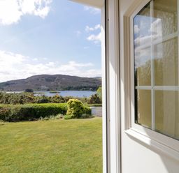 View of a lawn garden hedge and hill across a lake seen through an open door at LOCH ILLION VIEW in Dungloe County Donegal