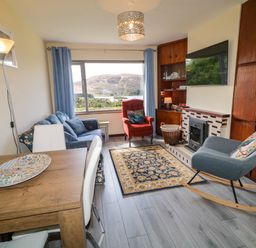 A living room with a wooden dining table white chairs blue sofa red armchair rocking chair and a fireplace at LOCH ILLION VIEW in Dungloe County Donegal