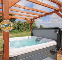 An outdoor hot tub under a wooden pergola with string lights and a sign that says Welcome to the hot tub sit back and relax at Barn Owl in Lode near Bottisham