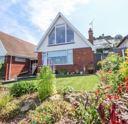 A brick house with white upper facade and large windows with a front garden at 67 Pendre Avenue in Prestatyn