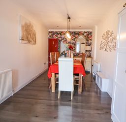 A dining room with a wooden dining table covered with a red tablecloth and wooden chairs in front of a floral wallpapered wall at 67 Pendre Avenue in Prestatyn