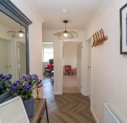 A hallway with a large mirror and flowers on a console table a light fixture on the ceiling and two chairs visible in rooms beyond at Hillside in Bishops Cleeve