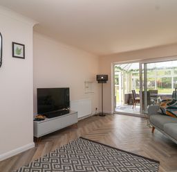 A living room with a TV on a stand a patterned rug a sofa with cushions sliding doors to a conservatory at Hillside in Bishops Cleeve