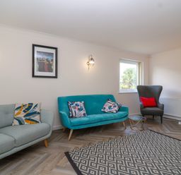 A living room with two sofas a patterned rug a window and wall lights at Hillside in Bishops Cleeve