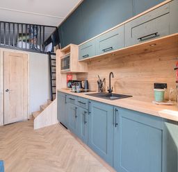 A kitchen area with blue cabinets, wooden countertop, sink, microwave, kettle, coffee maker, utensils and a loft bed accessed by a ladder at Starlight Skylight - Billing Aquadrome in Billing Aquadrome Holiday Park