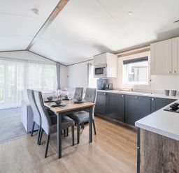 A kitchen and dining area with a wooden dining table set for four chairs and kitchen cabinets at Lakeside Lullaby Billing Aquadrome Holiday Park