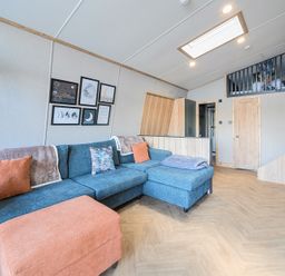 A living area with a blue sectional sofa and orange ottoman under framed wall art and a skylight at Moonlit Skylight - Billing Aquadrome in Billing Aquadrome Holiday Park