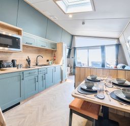 A kitchen and dining area with blue cabinets, a wooden dining table set for four, and large windows at Moonlit Skylight - Billing Aquadrome in Billing Aquadrome Holiday Park