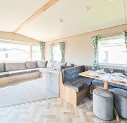 An interior living area with grey sofas and a wooden dining table set with white plates and glasses at Willowbrook Hideaway - Billing Aquadrome in Billing Aquadrome Holiday Park