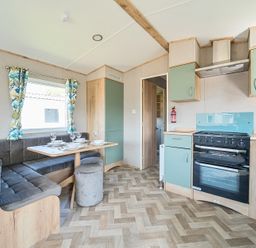 A kitchen and dining area with green cabinets a stove and a corner sofa with a table at Brookside Bliss - Billing Aquadrome in Billing Aquadrome Holiday Park
