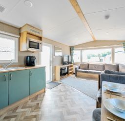 An open plan living area with kitchen, dining table, sofa, and television at Brookside Bliss - Billing Aquadrome in Billing Aquadrome Holiday Park