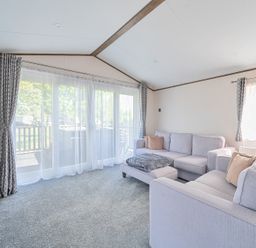 A living room with two sofas a footstool a television and large windows with curtains at Wave Whisperers - Hayling Island in Hayling Island Holiday Park