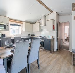 A kitchen with dining table and chairs next to a doorway showing a bedroom at Wave Whisperers - Hayling Island Holiday Park