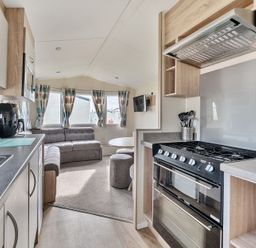 A kitchen and living area with cabinets stove microwave sofa and dining table at Golden Dune - Hayling Island in Hayling Island Holiday Park
