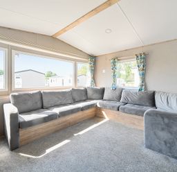A living room with a large gray corner sofa and windows with floral curtains at Sunset Sands - Hayling Island in Hayling Island Holiday Park