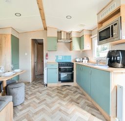 A kitchen with teal and wood cabinets a dining table with place settings and chairs at Sunset Sands - Hayling Island Hayling Island Holiday Park