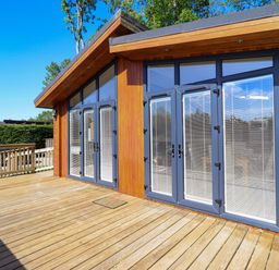A wooden deck with glass doors and blinds on a wooden building at Kingfisher Lodge in Gargrave