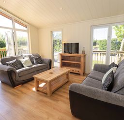 A living room with two gray sofas a wooden coffee table a wooden TV stand and large windows at Kingfisher Lodge in Gargrave