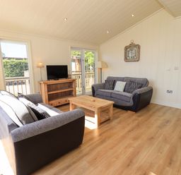 A living room with two sofas a wooden coffee table a television on a stand and large windows at Kingfisher Lodge in Gargrave
