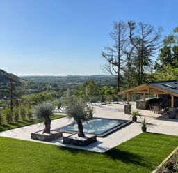An outdoor area with a pool two trees on stone bases a covered seating area and green lawn at Forest View in Pontyclun