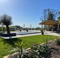 An outdoor space with a swimming pool surrounded by plants and trees and a covered seating area at Forest View in Pontyclun