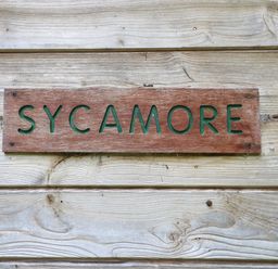 A wooden sign with the word sycamore on a wooden wall at Sycamore Lodge in Rosliston