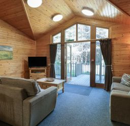 A living room with two sofas a wooden coffee table a television on a stand and large glass doors leading outside at Cedar Lodge in Rosliston