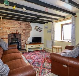 A living room with two brown sofas and a colorful rug in front of a brick fireplace at Rock Cottage in Portmellon near Mevagissey