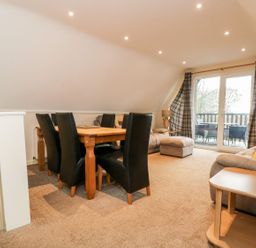 A dining area with a wooden table and black chairs next to a living space with sofas and a balcony at Valley Lodge 31 in St Ann's Chapel Cornwall