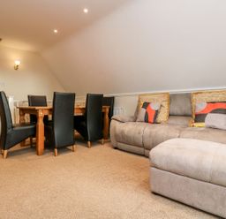 A living room with a gray sofa and ottoman with patterned cushions and a wooden dining table with black chairs at Valley Lodge 31 in St Ann's Chapel Cornwall