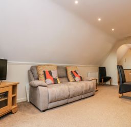 A living room with a sofa a TV on a wooden stand a wooden dining table with black chairs and an arched doorway at Valley Lodge 31 in St Ann's Chapel Cornwall
