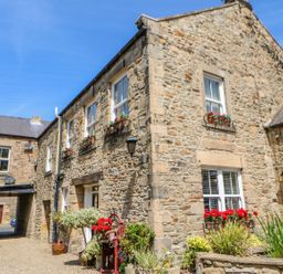A stone building with multiple windows and flower boxes outside a courtyard at Shaftoe Mews in Haydon Bridge