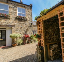 A courtyard with stacked firewood a stone house flower pots and gravel ground at Shaftoe Mews in Haydon Bridge