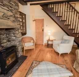 A living room with a fireplace and wooden stairs at Stoker’s Cottage in Bowness-On-Windermere