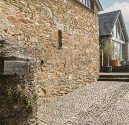 An outdoor area with a stone wall and a sign at Lower Velwell Barn in Totnes