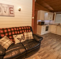 A living room with a sofa and kitchen area at Farnes Lodge Longframlington
