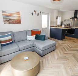 A living room with a sofa and kitchen area at Seahorse Cottage in Chathill