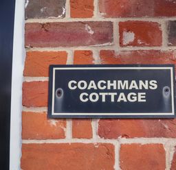A sign that says COACHMANS COTTAGE on a brick wall at Coachman's Cottage Ipswich