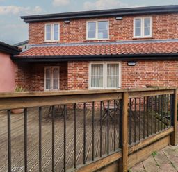 An outdoor area with a wooden deck and a two-story brick building at Blacksmith's Cottage Ipswich