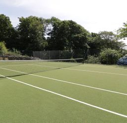 A tennis court with net and greenery at Bwthyn Canol in Llanfair