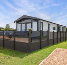 A caravan with a surrounding fence and grass area at Hazelnut Lodge in Chipping Norton