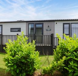 A mobile home with a deck and bushes at Hazelnut Lodge in Chipping Norton