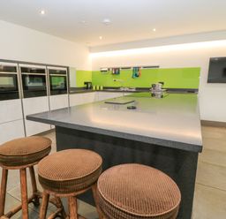 A kitchen with stovetop, stools, ovens and sink at Silver Copse Frilford Heath Near Abingdon