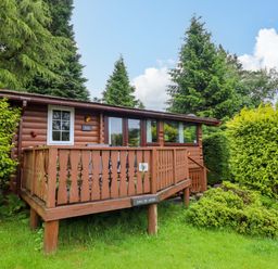 A log cabin with a deck and surrounding greenery at Swn Yr Afon - No 333