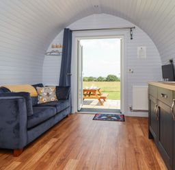 A living room with a sofa and door leading to an outdoor area at Honeypot Hideaways - Clover