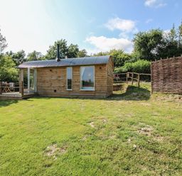 A wooden cabin with a deck and fence at Squirrel's Drey, Chapel Lawn near Clun