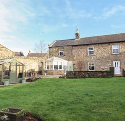 A garden with a greenhouse and building at Linn Cottage in Hexham