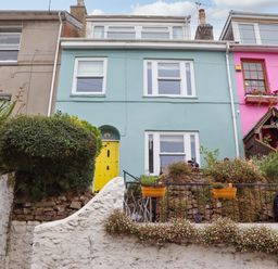 A colorful house with a yellow door and plants in pots at Captains Cottage in Brixham